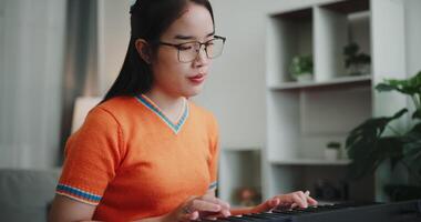 Young Asian woman is relaxing and enjoying playing music on an electronic keyboard in a quiet house. Leisure activities at home video