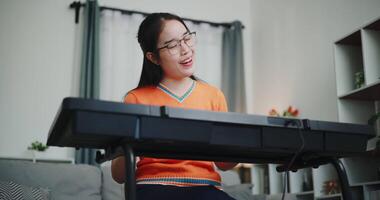 Handheld low angle view shot, Asian woman playing the keyboard with happy smile in cozy living room. Enjoy a relaxing weekend activity video