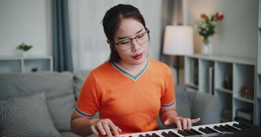Young Asian woman is relaxing and enjoying playing music on an electronic keyboard in a quiet house. Leisure activities video