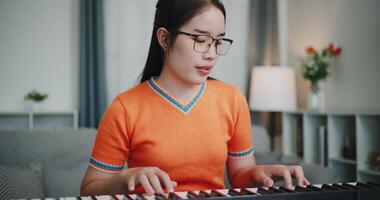 Medium shot, Young Asian woman is relaxing and enjoying playing music on an electronic keyboard in a quiet house. Leisure activities at home video