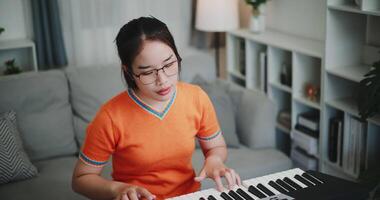 Beautiful Asian woman playing the keyboard with happy smile in cozy living room. Enjoy a relaxing weekend activity video