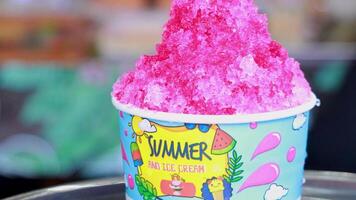 Bright pink shaved ice in a colorful cup, captured in a lively outdoor setting with dynamic camera angles video