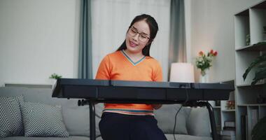 Handheld shot, Asian woman playing the keyboard with happy smile in cozy living room. Enjoy a relaxing weekend activity video