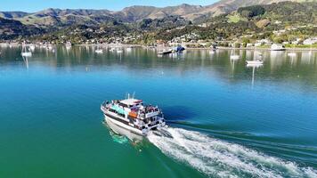 Aerial view of a boat cruising through Akaroa's serene bay, surrounded by lush hills and clear skies video