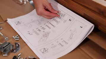 Hands follow detailed instructions to assemble furniture using screws and bolts on a wooden surface video