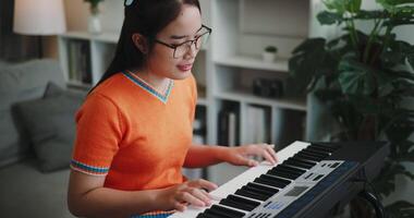 Handheld shot, Beautiful Asian woman playing the keyboard with happy smile in cozy living room at home. Enjoy a relaxing weekend activity video