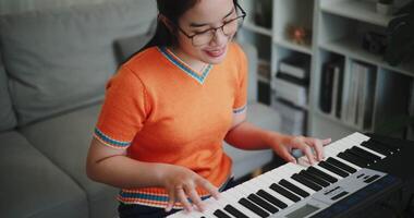 Handheld high angle view shot, Asian woman playing the keyboard with happy smile in cozy living room. Enjoy a relaxing weekend activity video
