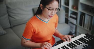 Asian woman is relaxing and enjoying playing music on an electronic keyboard in a quiet house. Leisure activities at home video
