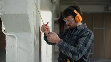 Builder using measure ruler writing mark on wall construction site Caucasian man holding measuring tool male guy foreman repairman handyman engineer architect industrial worker checking measurements video