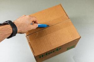 Lviv Ukraine 10.04.25 Opening a delivery box with a cutter on a grey table photo