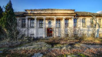 Abandoned neoclassical building in Schonebeck, Germany, with weathered columns and vegetation in the foreground photo