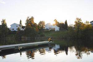 Lone man sits on pier an Oslo lake, Holmendammen as the sun sets behind charming houses, capturing a peaceful moment of reflection and stillness in Norway autumn magic photo