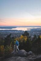 Traveler stands on a stump overlooking Oslo slowly falling asleep under the setting sun, as everything turns orange and pink. View from Vettakolltoppen, Norwegian nature photo