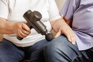 Elderly Using Percussion Massage Gun on Knee Pain Relief and Recovery with Electric Handheld Massager photo