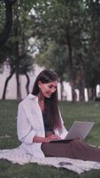 Online conference. The speaker girl is talking on a connection on a laptop, sitting on the grass in the park. Teacher. The coach advises clients on a call. Vertical format for the phone. video
