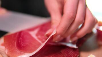 female hand separating slices of ham from packaging serving on wooden board. Cured raw ham, spinning. Slices of prosciutto crudo, Italian food. Pork dried ham. Antipasto, cold cuts. 4k . video