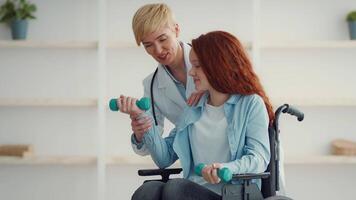 A healthcare professional supports a girl in a wheelchair as she engages in physical therapy exercises using light weights. The setting is bright and welcoming, promoting rehabilitation. video