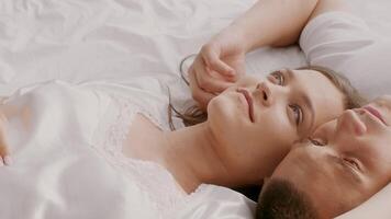A young couple lies in bed, enjoying a peaceful moment together. They express affection through gentle touches and soft glances, highlighting their loving relationship. video