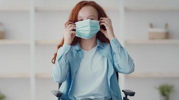 A young girl with red hair sits in a chair in a stylish room. She carefully adjusts her face mask, preparing for an outing or activity, showcasing a focus on health and safety. video