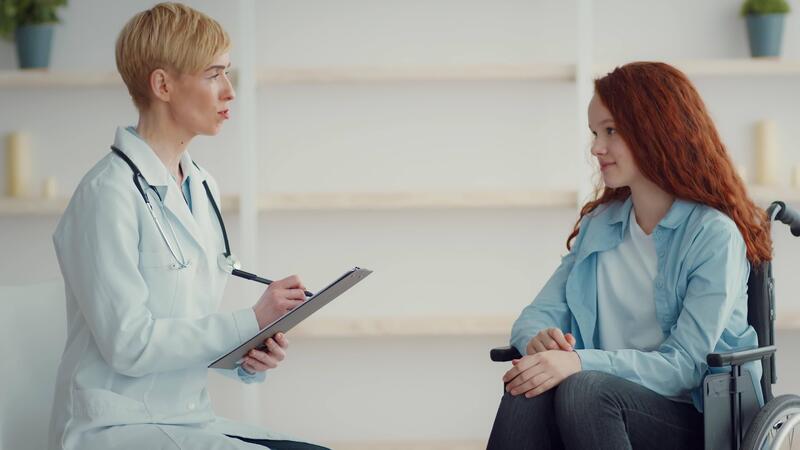 A healthcare professional in a - A Healthcare Professional In A White Coat Conducts A Consultation With A Girl In A Wheelchair They Are Discussing Health Issues In A Bright And Welcoming Clinic Environment Video 