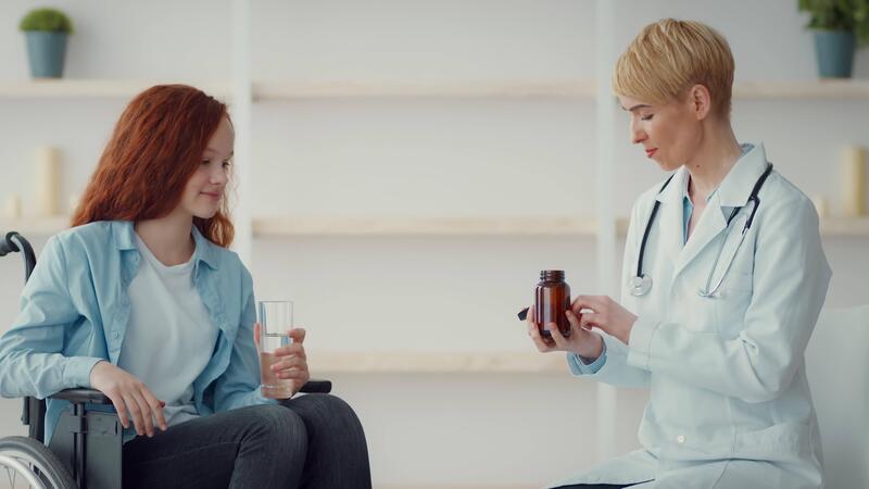 A healthcare professional wearing - A Healthcare Professional Wearing A Lab Coat Explains Medication To A Girl Sitting In A Wheelchair While Holding A Glass Of Water The Setting Is Bright And Welcoming Video 
