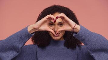 Smiling woman making heart gesture with hands on pink background video
