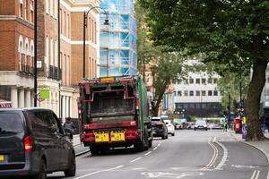 A green garbage truck navigates a London street, symbolizing the city dedication to sustainability amid a backdrop of classic British architecture... photo