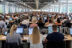 A large group of people sitting at desks in an office photo