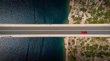 Top down view of a red car alone driving on a bridge over the sea. Background images for travel, holidays, the beauty of traveling by car to discover a country. Maslenica bridge, Croatia. photo