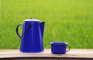 Kettle, blue enamel, and coffee mugs On an old wooden floor, Blurred background of rice fields at sunrise. photo