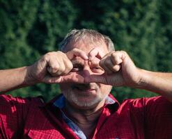 Playful Senior Man Making Heart Shape with Hands in Front of Face photo