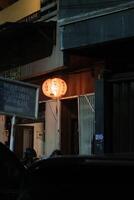 A red lantern hangs outside a building, casting a warm glow on the surrounding area. A sign in Indonesian reads Masuk Gedung Parkir Enter Parking Building. photo