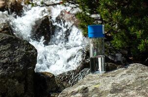 a clear glass bottle on a stone in front of mountain river steam photo
