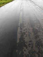 Failing road surface in Wales, showing deterioration, construction site, rain-wetted tarmac. photo