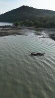 Vertical Aerial view of wooden boat speeding through a blue tropical lagoon, scenic landscape of a sailboat on crystal clear water. Thai paradise of lush coastal cliffs and small islands. video