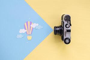 Summer and travel concert. Air balloon with clouds cut out of paper. Camera on a yellow-blue pastel background. Top view photo