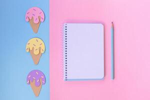 Notebook with pencil on a pink and blue background and ice creams. Background with cut out paper ice creams. Summer concept. Top view, space photo