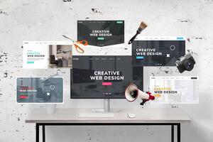 Web pages flying around a web designer's desk and computer display featuring an agency web page presentation. Includes web designer tools, megaphone, wrench key, photo camera, scissors, and brush