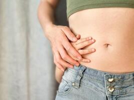 Close up of woman in jeans and green top with childs hands on her belly. Concept of family bonding, motherhood, postpartum recovery, mother love and affection. Neutral background photo