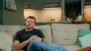 Man resting on sofa, holding TV remote control in hand. Person relaxing on couch and watching television. Concept of relaxation, leisure time and home entertainment video