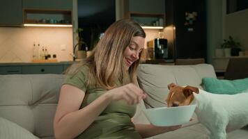Woman relaxing on sofa with remote control while dog steals food. Pet dog eat food from bowl while owner focuses on TV. Pet behavior concept video