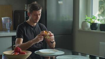 Man eating sesame bagel with egg, cheese and ham in kitchen. Person has breakfast with homemade sandwich video