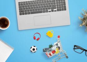 Shopping cart on a desk with products around it and a laptop computer beside. Concept of online shopping and digital retail photo