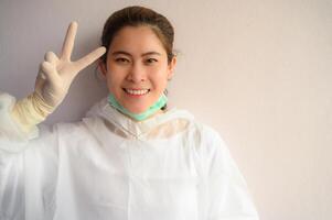 Asian Nurse wearing PPE suit and showing V sign or Victory sign. In coronavirus pandemic outbreak we should support and encourage healthcare worker by stay home and listen to medical advice. photo