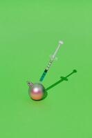 Pink Christmas bauble changing color into tiffany blue by injection on green background. Creative Christmas and New Year concept. Minimal surreal medical Christmas layout. Xmas aesthetic. photo