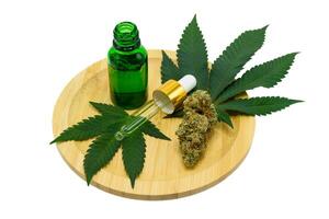 Cannabis flower buds with green dropper bottle and green leaf on a wooden plate on white isolated background, Scientists research CBD and THC extract oil from marijuana in pharmaceutical industry. photo