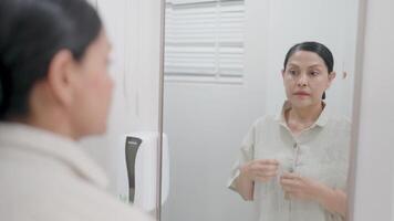 A middle-aged woman stands in front of a mirror to record a moment of private reflection. video