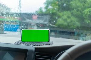 Smartphone with Green Screen on Dashboard in Rainy Car photo