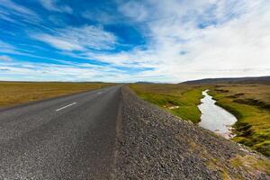 Highway through Icelandic landscape under a blue summer sky with clouds photo