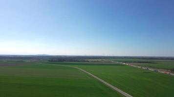 Aerial view of green agricultural landscape with farmland, highway and wind turbines in background. Concept of eco transport, rural logistics and sustainable infrastructure video